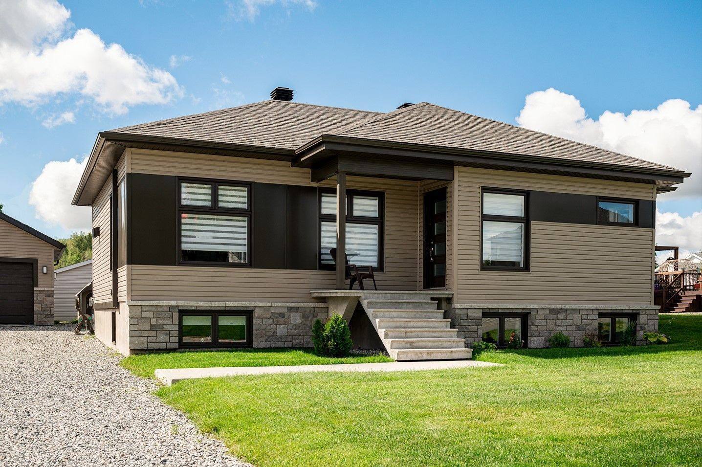 Un bungalow Maison Nordique : revêtement gris et brun, toiture noire, pelouse fraîchement tondue